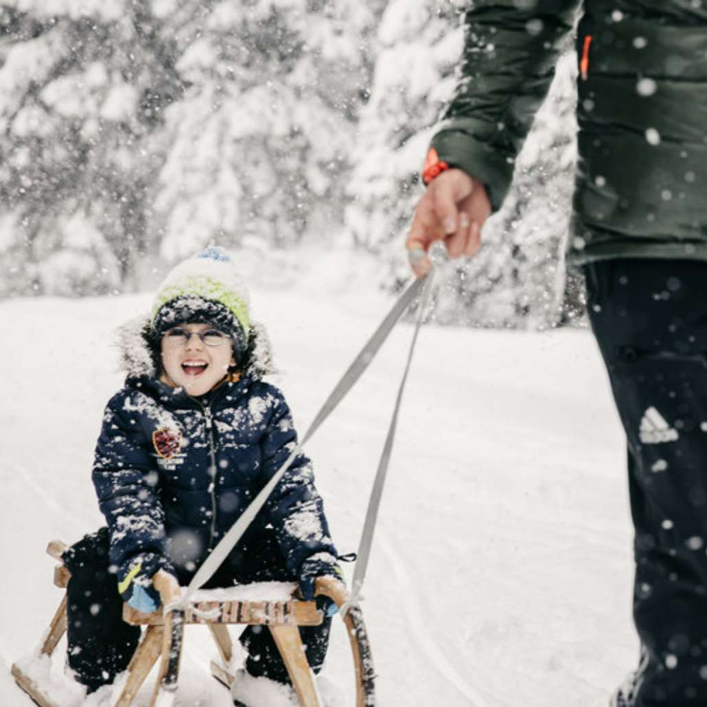 Aktiv mit der ganzen Familie Fröhliches Kind wird auf einem Schlitten durch den Schnee gezogen