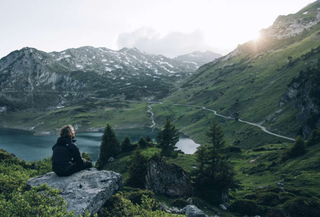 Atemberaubender Ausblick Person sitzt bei Sonnenaufgang auf einem Felsen und genießt die Aussicht auf die Berglandschaft.