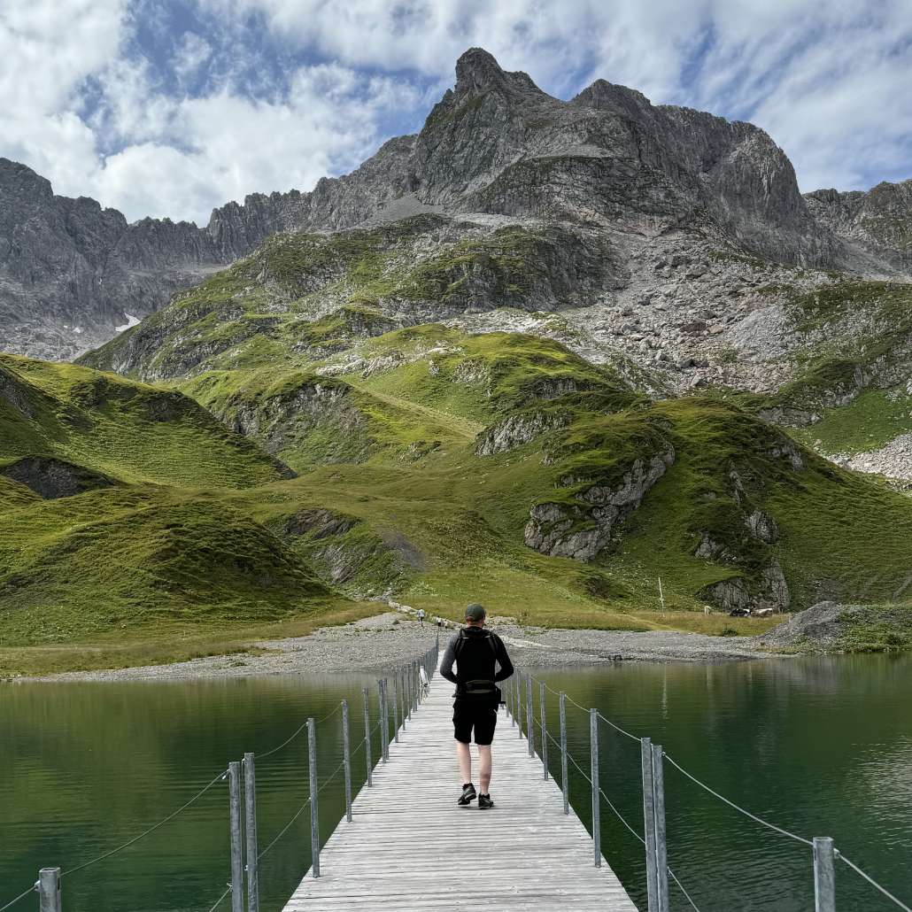 Wandertage Arlberg Person auf einer Brücke wandert den Bergen entgegen
